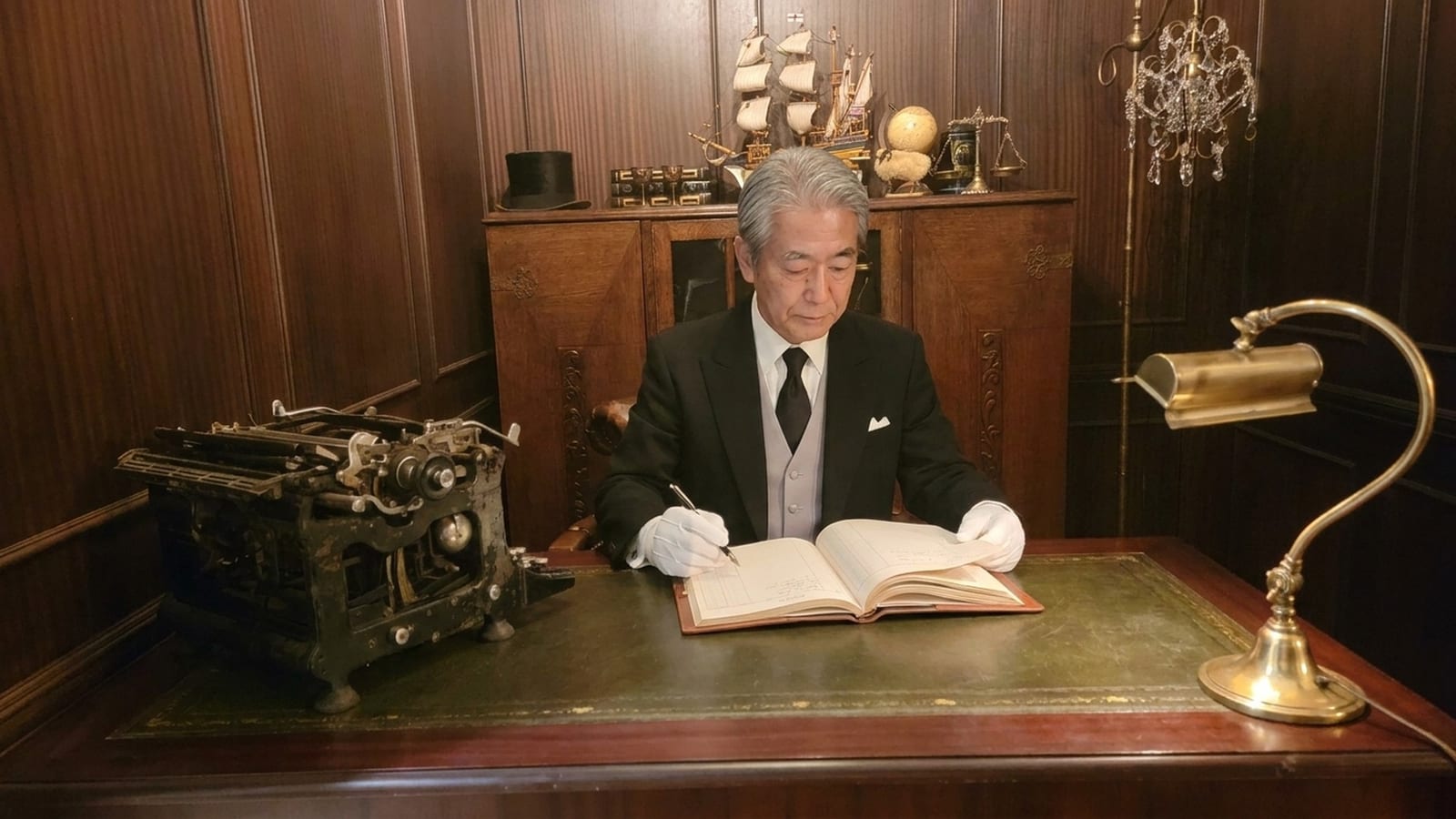 日本執事アカデミーの公式サイトより。書斎の机で年長の執事が教本を開き、マスター課程の学びに向かう場面